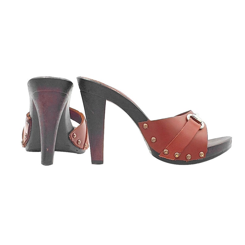 K&ouml;nnte beinhalten: Ein Paar braune Ledersandalen mit Absatz und einer silbernen Schnalle. Die Sandalen haben eine Holzplattform und einen hohen Absatz.