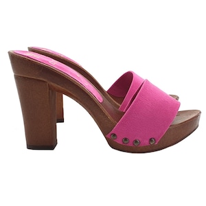 May include: A pair of pink suede open-toe platform heels with wooden soles and heels. The heels are approximately 4 inches tall. The shoes have a strap across the top of the foot and are secured with small metal studs.