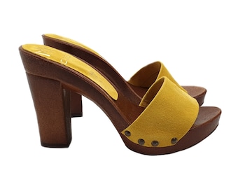 May include: Yellow suede heeled clogs with a wooden platform and brown block heel. The clogs have a studded design on the front.