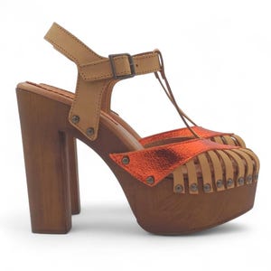 May include: Platform sandals with a wooden base and heel. The sandals feature a tan leather strap and a metallic orange accent on the toe. The heel is approximately 10 cm high.