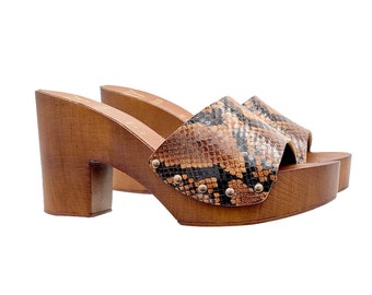 May include: Brown wooden platform clogs with a snake print leather upper. The clogs have a chunky heel and a pointed toe.