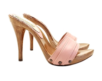 May include: A pair of pink leather heeled clogs with a wooden platform and a stiletto heel. The clogs have a single strap across the top of the foot and are secured with a buckle.