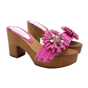 May include: Pink suede clogs with a wooden platform and a large flower embellishment with rhinestones.