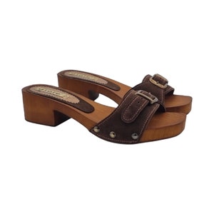 May include: Brown suede heeled clogs with a buckle closure and wooden platform. The clogs have a brown suede strap with a silver buckle and a wooden heel.