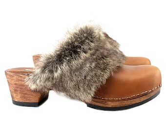 May include: Brown leather clogs with a wooden heel and a gray fur trim around the top.