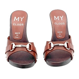 K&ouml;nnte beinhalten: Ein Paar braune Ledersandalen mit Absatz und einer silbernen Metallschnalle. Die Clogs sind in Italien hergestellt und tragen den Markennamen "MY CLOGS" auf der R&uuml;ckseite.