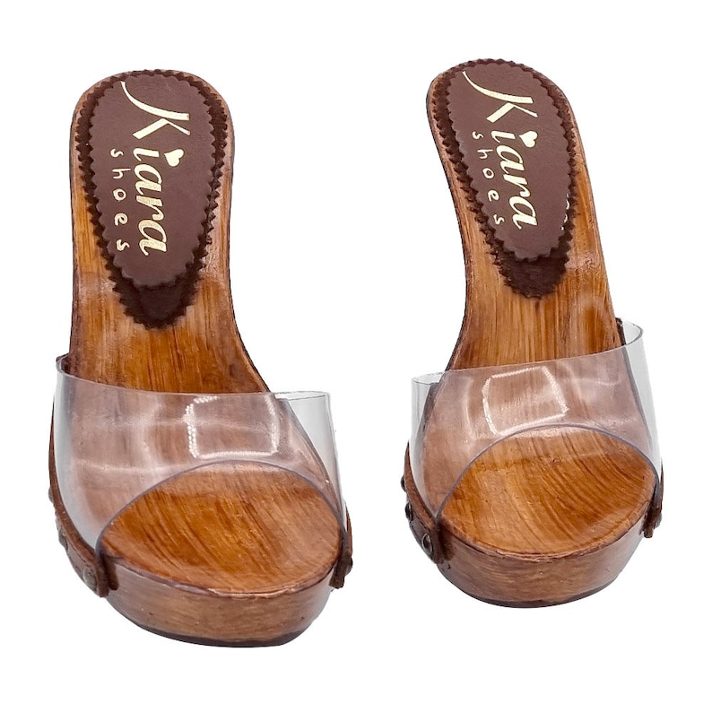 May include: Pair of brown wooden platform clogs with clear plastic straps and a gold "Kiara Shoes" logo on the insole.