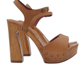 May include: Tan leather heeled sandals with a wooden platform and chunky heel. The sandals have a buckle closure and a peep toe.