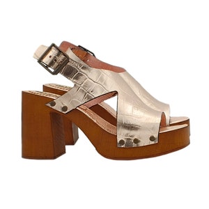 Peut inclure: Sandales plates en cuir doré avec un talon en bois et une fermeture à boucle. Les sandales ont un motif gaufré crocodile.