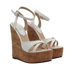 Puede incluir: Sandalias de cuña blancas con plataforma de corcho y tiras cruzadas. Las sandalias tienen una tira para el tobillo con cierre de hebilla.
