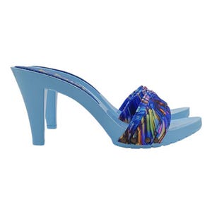 May include: Light blue high-heeled clogs with a vibrant, patterned fabric strap. The heels are a solid light blue, and the strap features a colorful design with shades of blue, yellow, and green. The clogs have a classic, open-toe design.