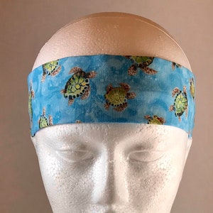 May include: A blue headband with a pattern of green sea turtles on a light blue background.