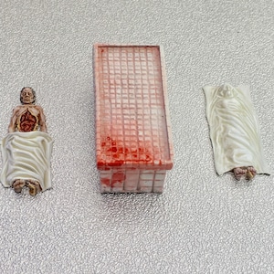 Morgue Slab & bodies 28mm RPG pewter 3 piece set: 1 morgue table, 1 body under sheet, 1 body chest open. “Sold unpainted”.