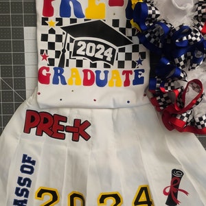 May include: White pre-k graduation outfit with a black and white checkered pattern, red, blue, and yellow accents, and the text "PRE-K 2024 GRADUATE". The outfit includes a white shirt, a white skirt with the text "PRE-K CLASS OF 2024" and a graduation cap.