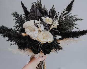 May include: A black and white dried flower bouquet with black roses, white roses, and black and white pampas grass.
