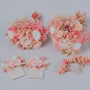 May include: A selection of pink and white floral arrangements, including two bouquets, two corsages, and a set of hair pins. The bouquets feature roses, baby's breath, and other delicate flowers. The corsages are attached to lace. The hair pins are adorned with small flowers.