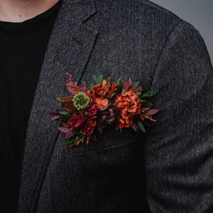 May include: A gray blazer with a floral boutonniere made of red, orange, and green flowers.