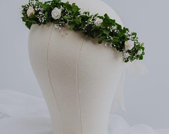 May include: A white flower crown with small white flowers and green leaves on a white mannequin head.