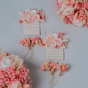 May include: Image of pink and white floral arrangements, including roses and baby's breath, against a light grey backdrop. The image shows several floral hair accessories and bouquets, ideal for weddings or special occasions.