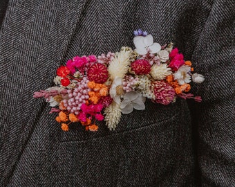 May include: A small bouquet of dried flowers in shades of pink, orange, and white, arranged in a pocket square.
