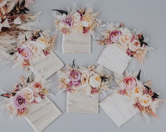 May include: Six small white boxes with delicate floral arrangements on top. Each arrangement features a mix of pink and cream colored flowers, dried grasses, and greenery.