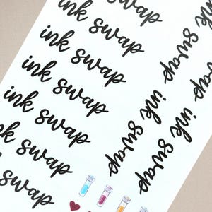 May include: A white sticker sheet featuring the repeating black cursive text ink swap arranged in multiple columns. At the bottom, there are small, colorful illustrations of test tubes filled with various liquids and a small dark red heart icon.