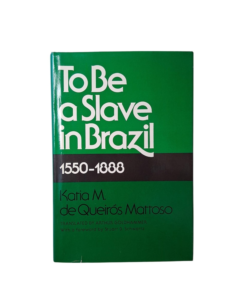 Puede incluir: Libro con portada verde y t&iacute;tulo "To Be a Slave in Brazil" en blanco. Tambi&eacute;n se ve el nombre de la autora, Katia M. de Queir&oacute;s Mattoso, y las fechas 1550-1888. Es un estudio hist&oacute;rico.