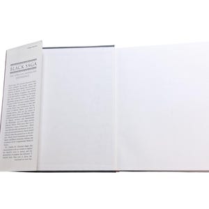 May include: An open book titled "Black Saga: The African American Experience." The book has a black cover and white pages. The title is printed in black and white. The book is open to show blank pages.