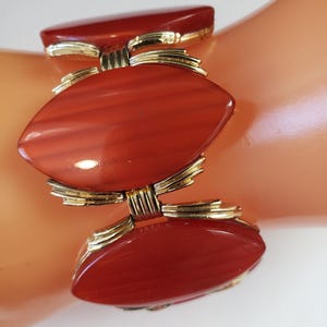 May include: A vintage bracelet featuring three oval, reddish-orange stones with gold-tone metal accents. The bracelet is composed of three linked segments, each with a central stone and decorative metalwork. The stones have a polished finish.