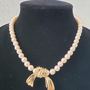 May include: A pearl necklace with a gold bow pendant. The pearls are cream colored and the bow is a classic design.
