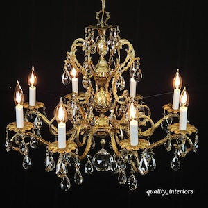 May include: Ornate gold chandelier with crystal accents and candle-style lights. The fixture has multiple arms with white candle-shaped bulbs and dangling crystal pendants. The design is elaborate and features floral and scrollwork details, creating a luxurious aesthetic.