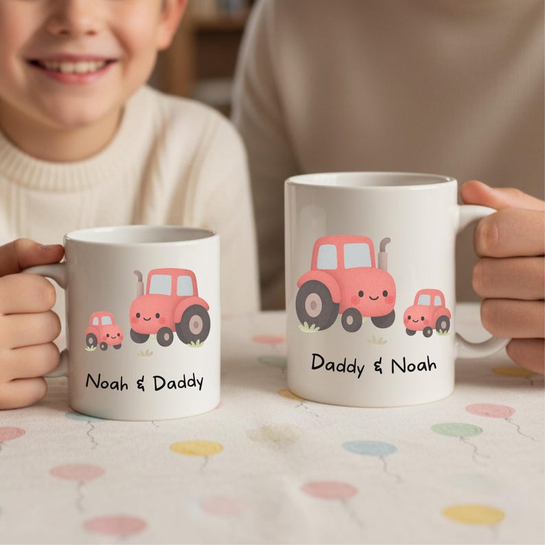 May include: Two white ceramic mugs featuring a cartoon tractor design. The tractors are red with black wheels and smiling faces. One mug says "Noah & Daddy", the other says "Daddy & Noah".