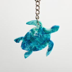 May include: A blue and green sea turtle keychain with a silver chain and ring. The turtle is made of resin and has a marbled effect.