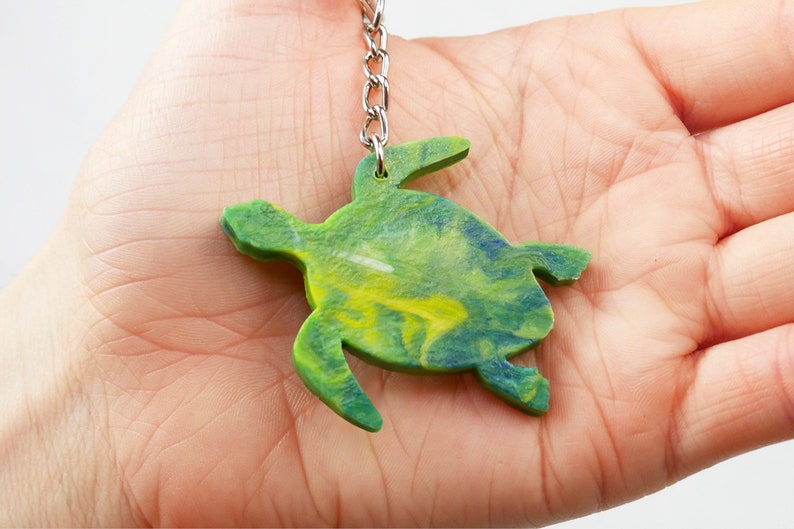 May include: A green, yellow, and blue sea turtle keychain made of resin. The turtle is on a silver chain.