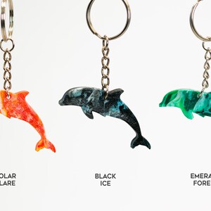 May include: Three dolphin keychains with different color patterns: orange and white, black and blue, and green and white. The keychains are labeled "Solar Flare", "Black Ice", and "Emerald Forest".