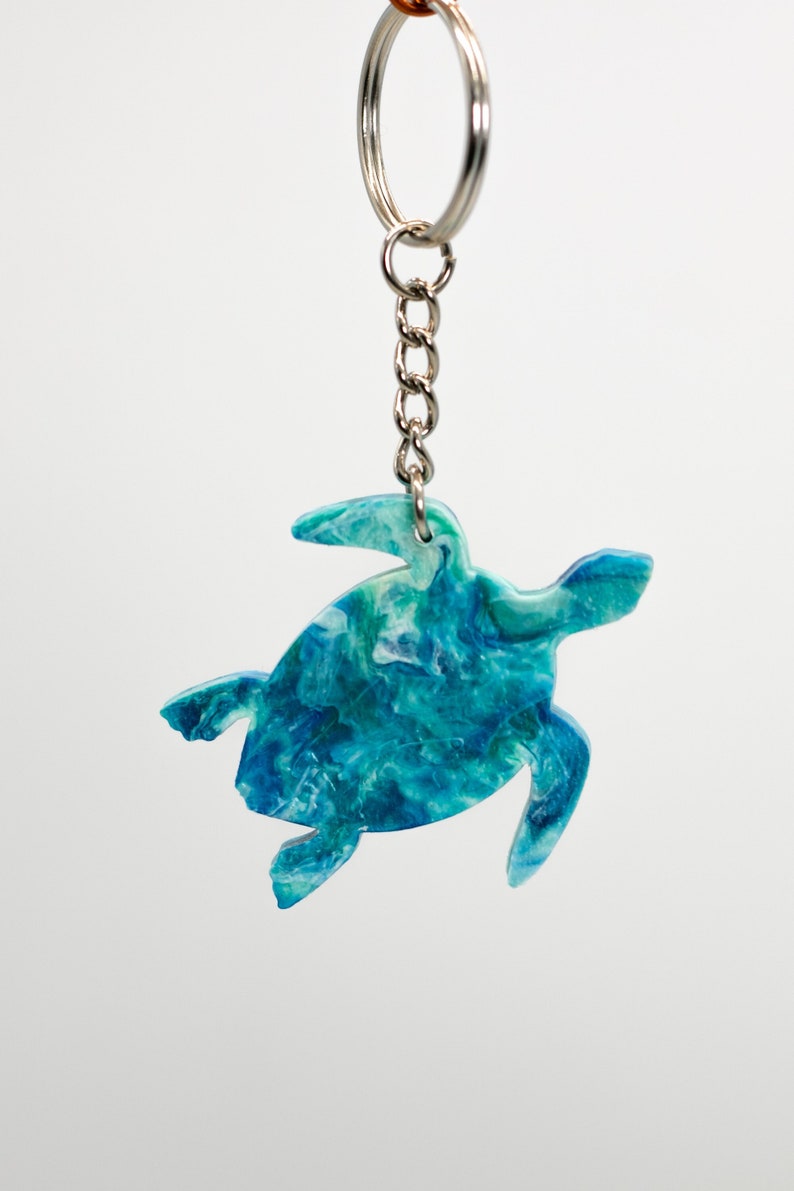 May include: A blue and green sea turtle keychain with a silver chain and ring. The turtle is made of resin and has a marbled effect.