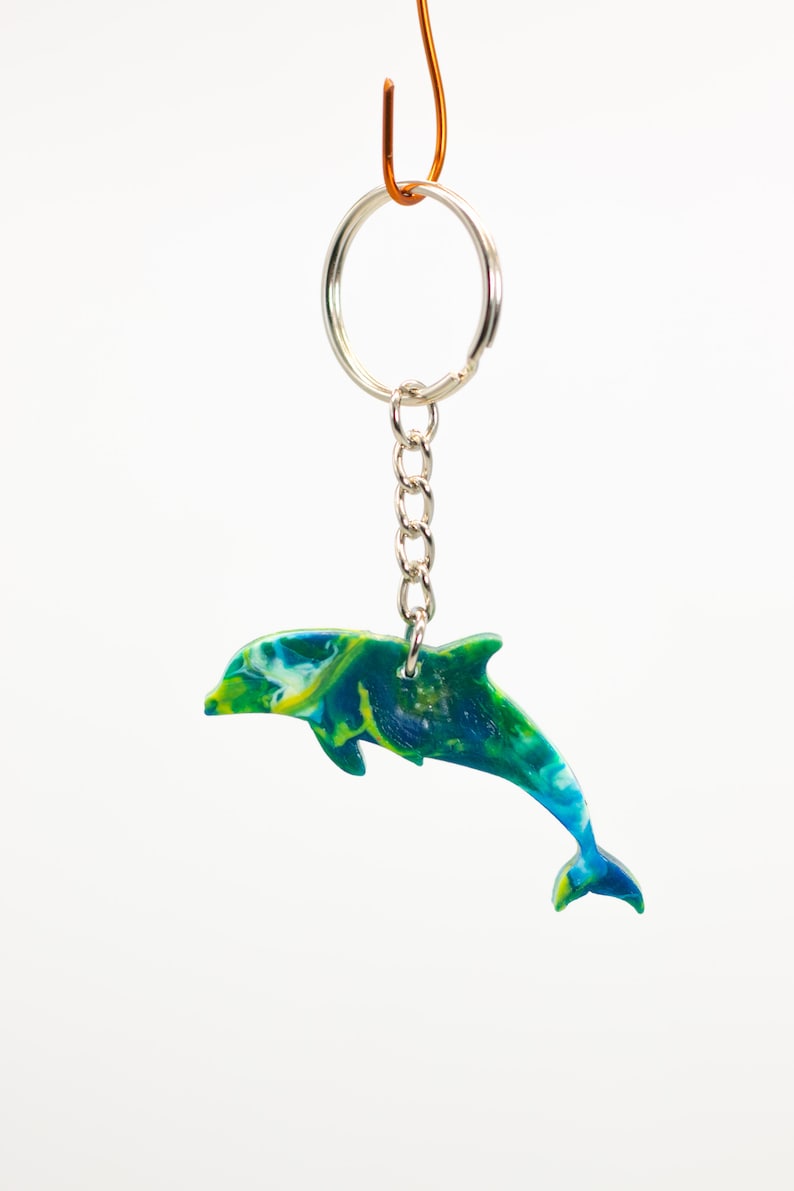 May include: A green, blue, and yellow dolphin keychain. The dolphin is jumping out of the water. The keychain is attached to a silver ring and chain.
