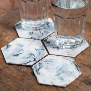 May include: Set of six hexagonal coasters with a white and blue marbled design. The coasters are made from a durable material and are ideal for protecting surfaces from spills and scratches.