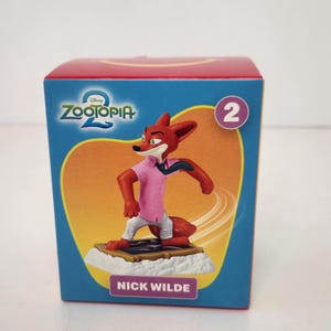 May include: A Zootopia 2 collectible figure of Nick Wilde, a red fox character, wearing a pink shirt and white pants. The figure is on a base and displayed on a blue box with the Zootopia 2 logo and the number 2.