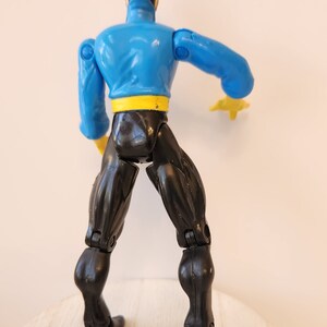 May include: A blue and black action figure with articulated limbs. The figure has a yellow belt and is posed with one arm raised.