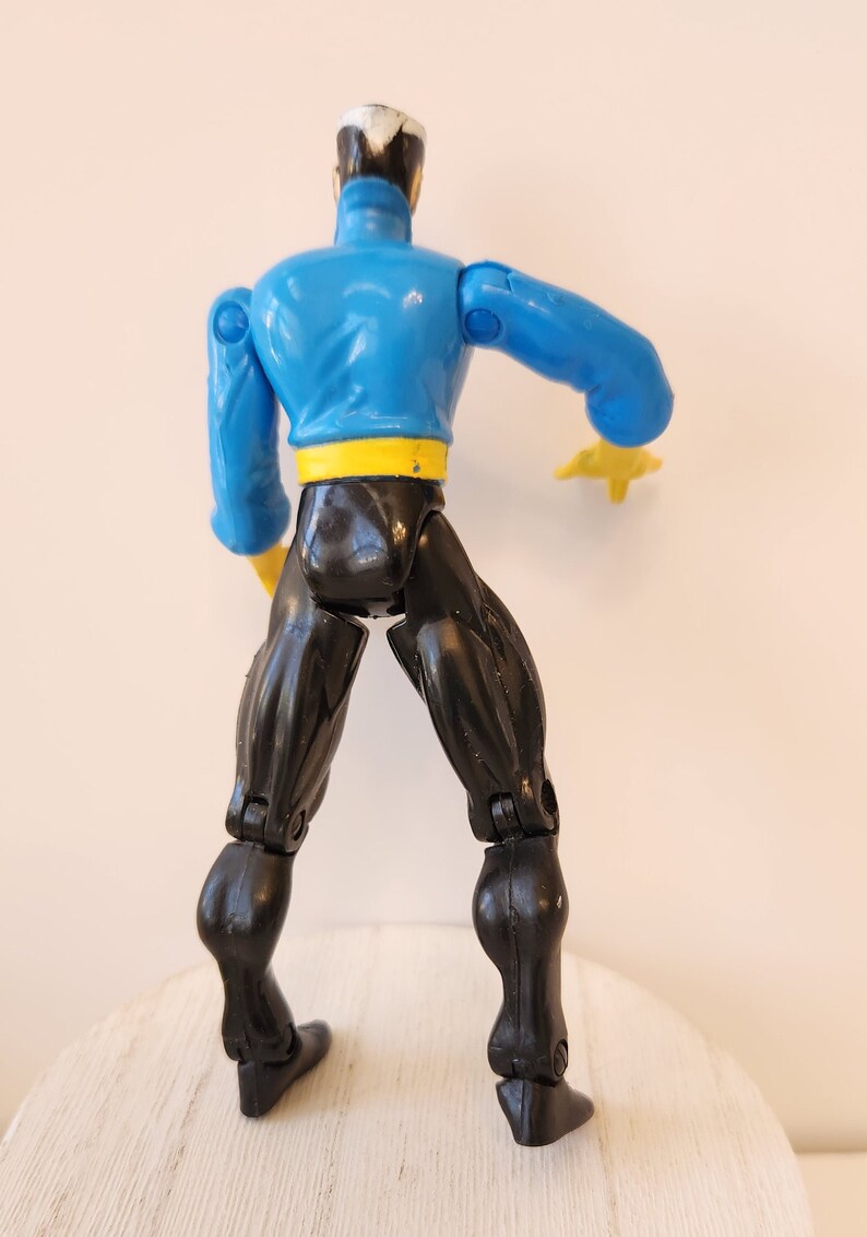 May include: A blue and black action figure with articulated limbs. The figure has a yellow belt and is posed with one arm raised.