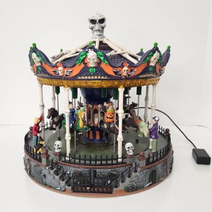 May include: A Halloween-themed carousel with a skull on top and skeleton-like supports. The carousel features figures of people and animals, with a spooky, festive design. The base has a fence and gate, with a power cord attached.