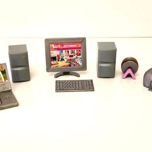 May include: A miniature grey computer set including a laptop with a screen graphic, a desktop monitor with a screen graphic, a keyboard, two speakers, a circular disc on a purple stand, and a printer. These plastic toy accessories are grey.