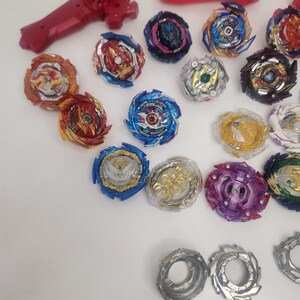 Puede incluir: Una colecci&oacute;n de coloridos trompos y lanzadores. Los trompos presentan varios dise&ntilde;os con acentos rojos, azules, dorados y morados. Tambi&eacute;n se incluyen un lanzador y un mango rojos, junto con componentes plateados y grises. Estos juguetes est&aacute;n dise&ntilde;ados para el juego competitivo.