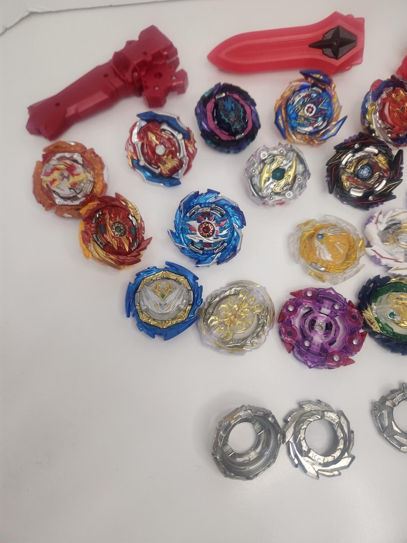 Puede incluir: Una colecci&oacute;n de coloridos trompos y lanzadores. Los trompos presentan varios dise&ntilde;os con acentos rojos, azules, dorados y morados. Tambi&eacute;n se incluyen un lanzador y un mango rojos, junto con componentes plateados y grises. Estos juguetes est&aacute;n dise&ntilde;ados para el juego competitivo.