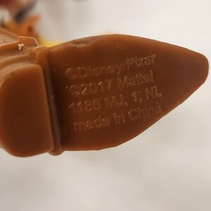 May include: Close-up of a brown plastic toy foot with text that reads "&copy;Disney/Pixar &copy;2017 Mattel 1186 MJ, 1, NL made in China". The toy foot is part of a larger toy figure.