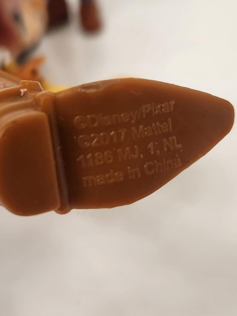 May include: Close-up of a brown plastic toy foot with text that reads "&copy;Disney/Pixar &copy;2017 Mattel 1186 MJ, 1, NL made in China". The toy foot is part of a larger toy figure.
