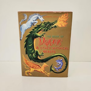 May include: A hardcover book titled The Book of Dragons & Other Mythical Beasts by Joseph Nigg. The gold cover features a white unicorn, a large green dragon breathing orange fire, a golden winged griffin, and a small blue sea creature.