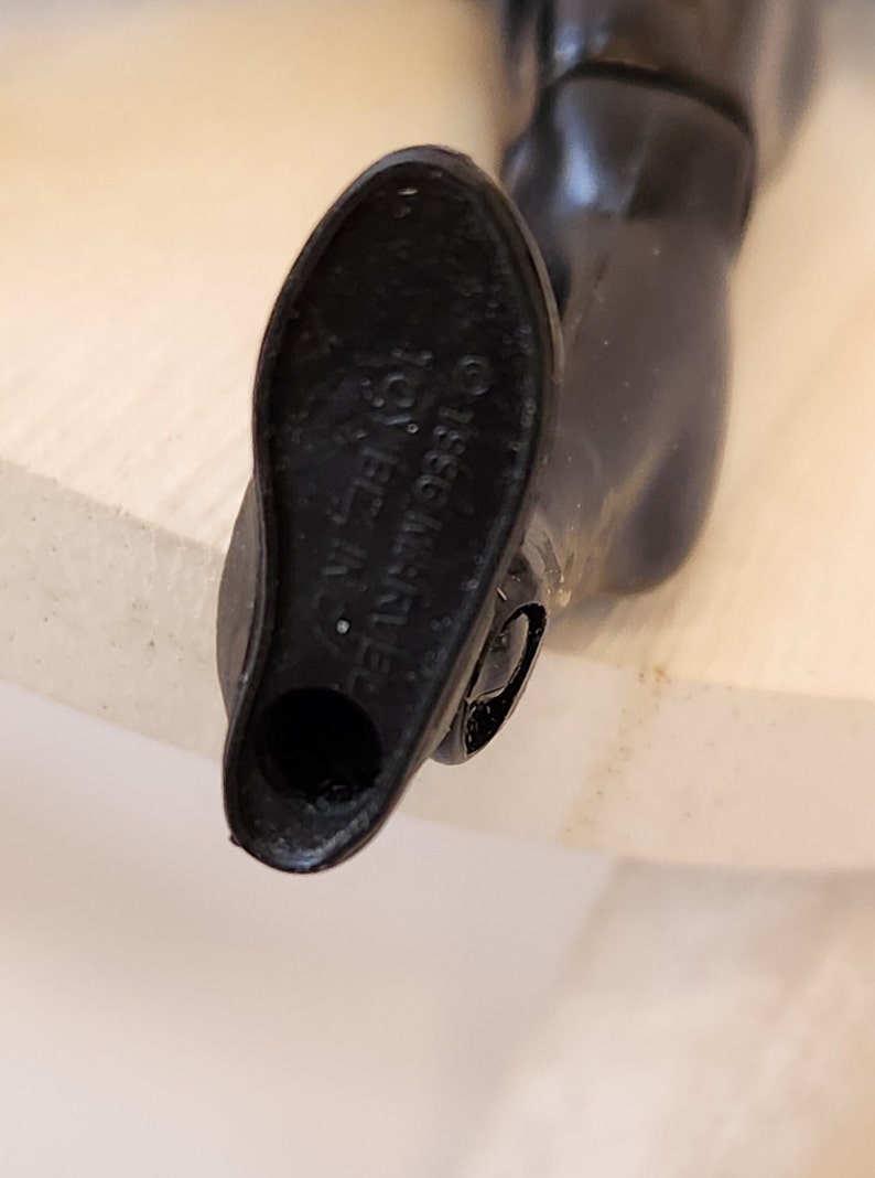 May include: Close-up of the bottom of a black plastic action figure leg. The bottom of the leg has a hole and the text "&copy;1983 Mattel, Inc."