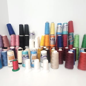 May include: A collection of colorful spools of thread in various shades, including blue, pink, green, and red. Some spools are stacked, while others are arranged in rows. The thread is likely for sewing or crafting.